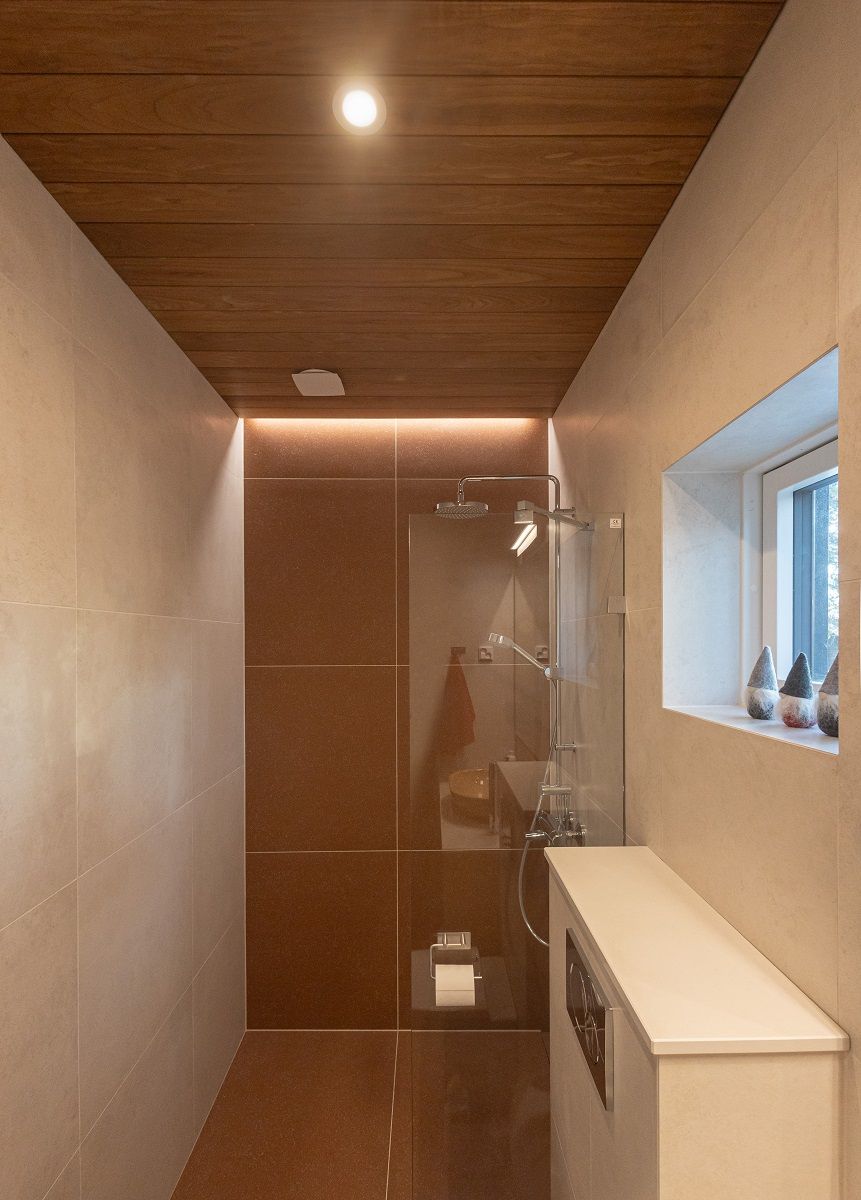 The back wall of the shower is accentuated by a uniform LED strip lighting and a flush spotlight as general lighting.